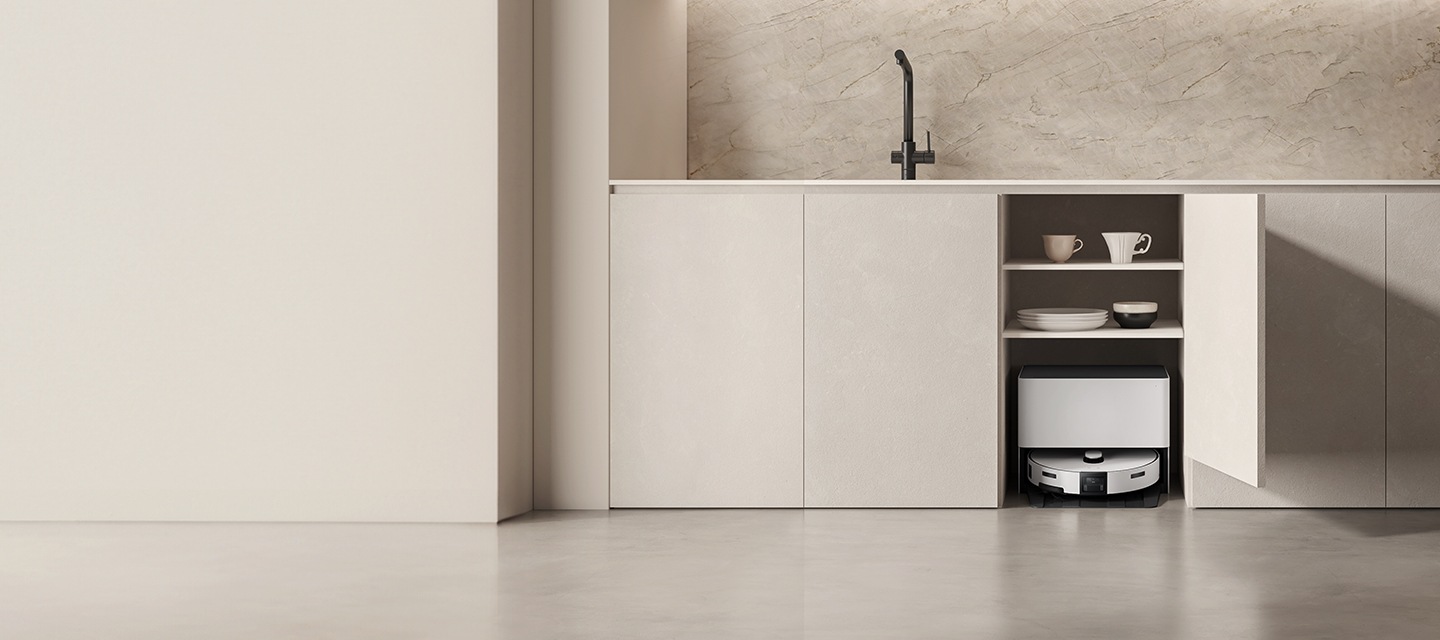 베이지톤 주방의 싱크대 하부 수납장 중 한 칸이 열려있고 그 안에는 컵과 그릇이,  최하단에는 Bespoke AI 스팀 울트라 자동 급배수 제품이 있다