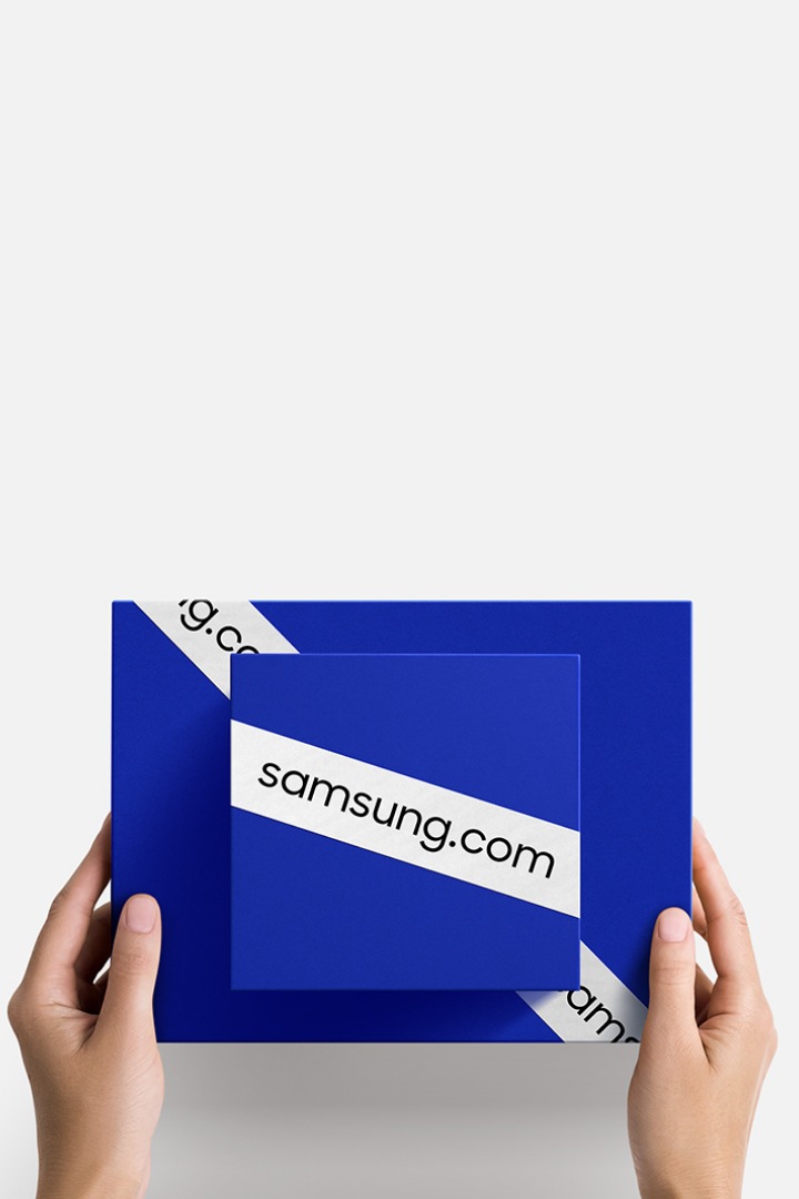 samsung.com 이라고 쓰인 띠가 둘러져 있는 파란색 상자 두 개를 겹쳐서 들고 있는 손이 보입니다.