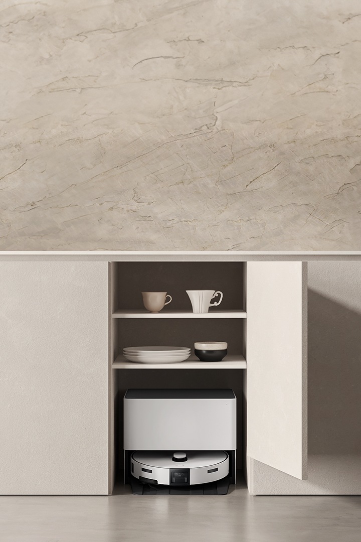 베이지톤 주방의 싱크대 하부 수납장 중 한 칸이 열려있고 그 안에는 컵과 그릇이,  최하단에는 Bespoke AI 스팀 울트라 자동 급배수 제품이 있다