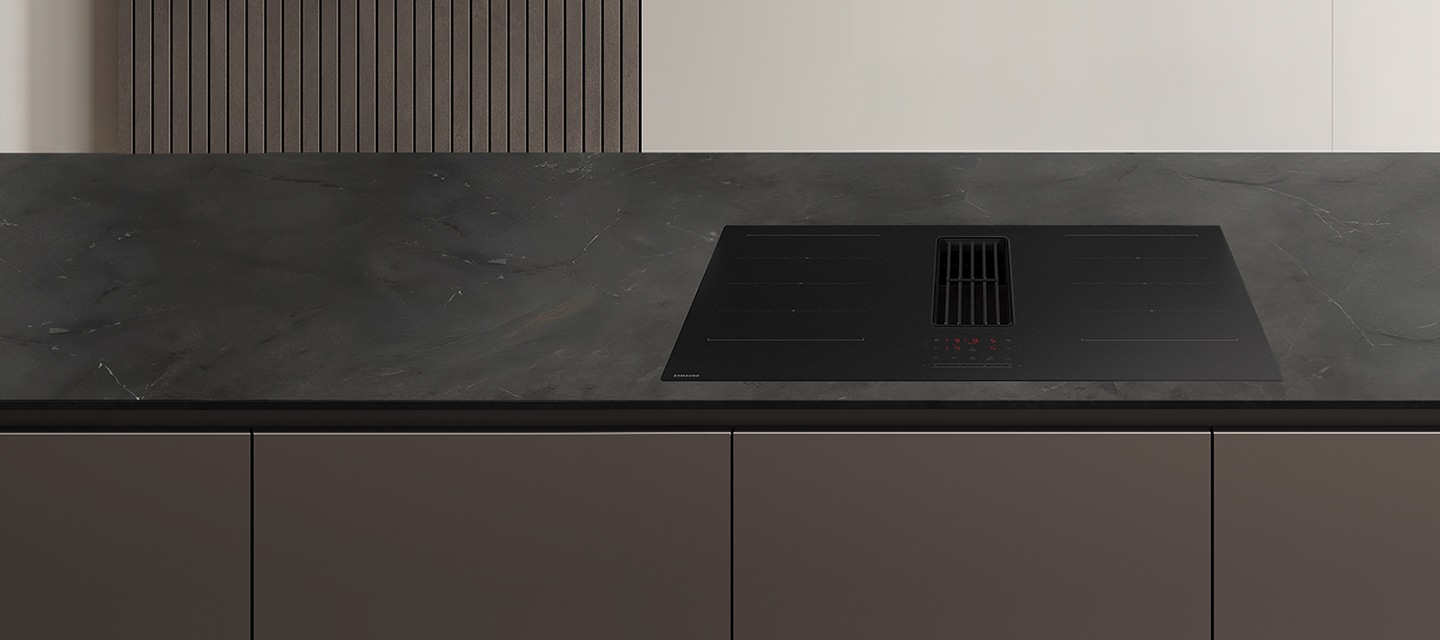 애쉬블랙색 대리석 아일랜드 테이블에 검정색 후드일체형 인덕션이 설치되어 있고, 아래는 고동색 빌트인 장이 보임