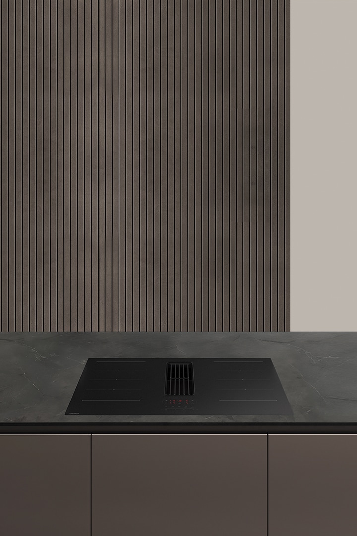 애쉬블랙색 대리석 아일랜드 테이블에 검정색 후드일체형 인덕션이 설치되어 있고, 아래는 고동색 빌트인 장이 보임