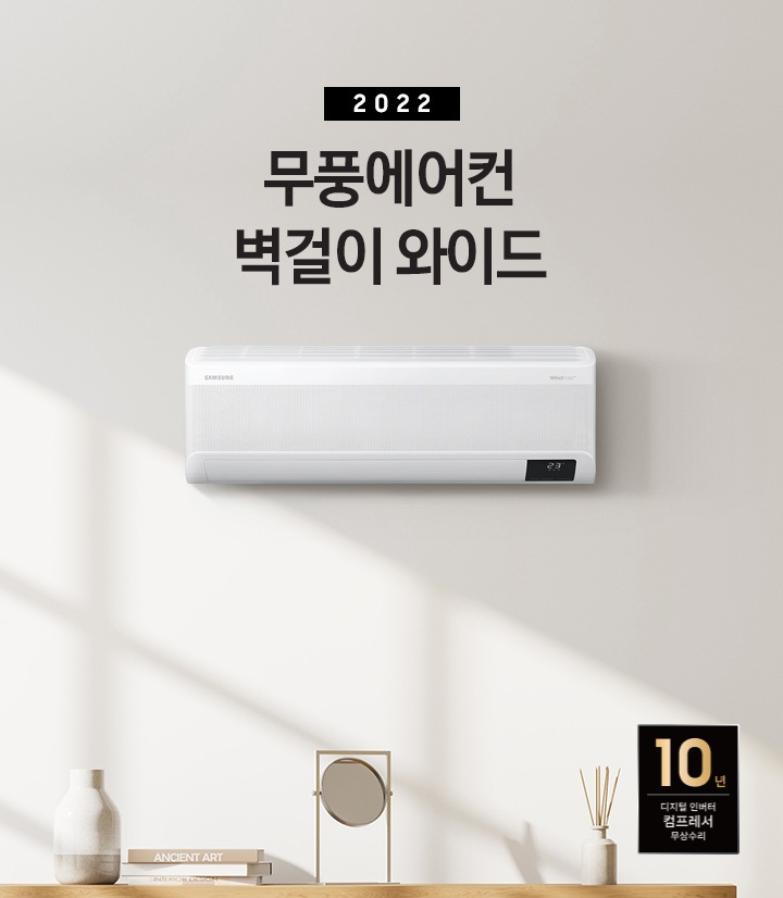 베이톤의 거실 공간이 보여지며 좌측 상단에 2022 무풍에어컨 벽걸이 와이드 문구가 보여지며 가운데 무풍벽걸이 와이드 에어컨이 설치 되어 보입니다. 좌측 하단엔 탁상의 위 부분만 보여지며 탁상 위 화병, 책, 거울, 디퓨저 순으로 보여집니다.  우측 하단에 10년 보증 디지털 인버터 모터&컴프레서 무상수리 마크가 보여집니다. 