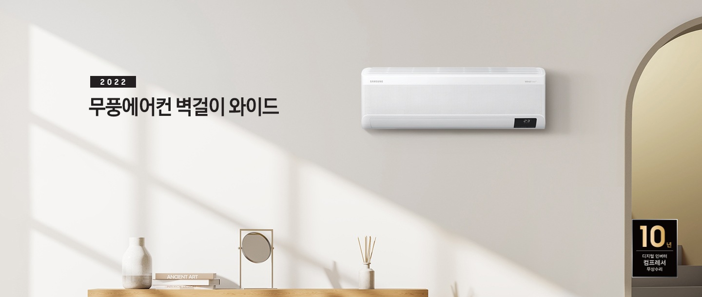 베이톤의 거실 공간이 보여지며 좌측 상단에 2022 무풍에어컨 벽걸이 와이드 문구가 보여지며 가운데 무풍벽걸이 와이드 에어컨이 설치 되어 보입니다. 좌측 하단엔 탁상의 위 부분만 보여지며 탁상 위 화병, 책, 거울, 디퓨저 순으로 보여집니다.  우측 하단에 10년 보증 디지털 인버터 모터&컴프레서 무상수리 마크가 보여집니다. 