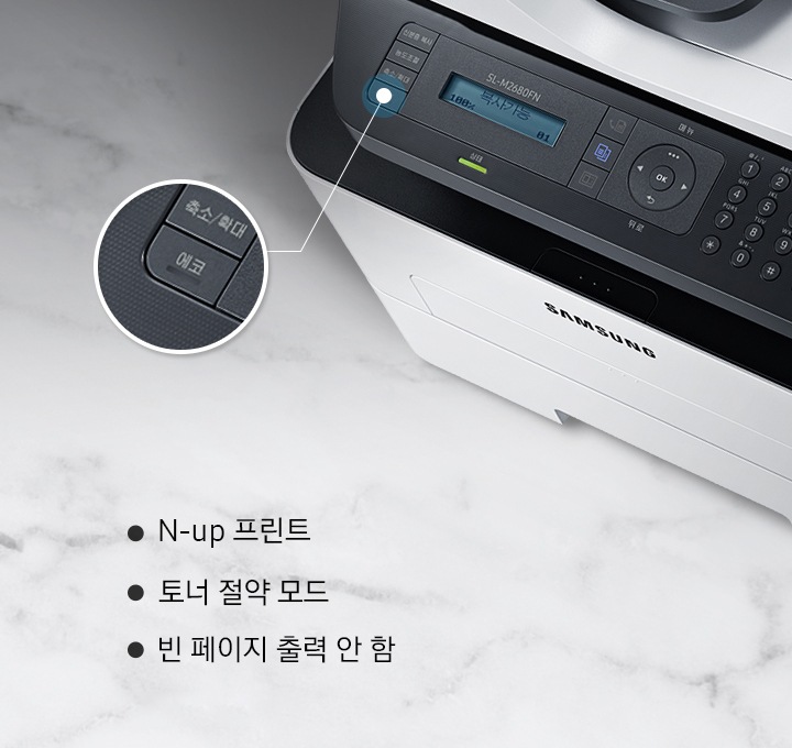 하얀 대리석 바닥에 이미지 오른쪽 위 부분에는 위에서 내려본 제품 이미지가 있고 제품 이미지에서 ECO 부분은 제품 이미지 왼쪽에 확대하여 보여주고 있습니다. 이미지 왼쪽 하단에는 N-up 프린트, 토너 절약 모드, 빈 페이지 출력 안 함 텍스트가 위에서 아래로 나열하여 있습니다.