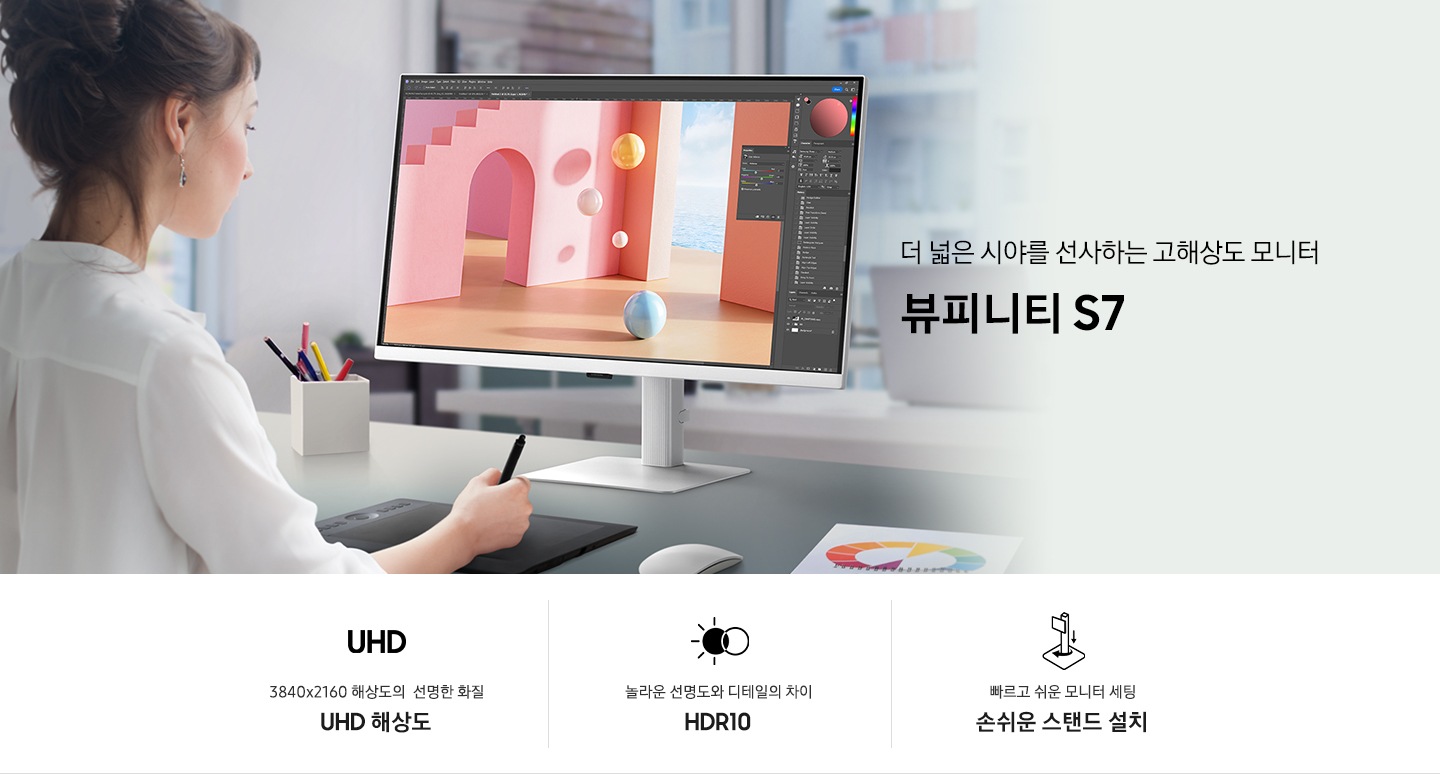 한 여성이 컴퓨터 앞에서 포토샵을 이용해 디자인 작업중인 모습이 보입니다. 데스크에는 모니터와 펜 타블릿, 연필꽂이와 색상샘플 등이 보입니다. 