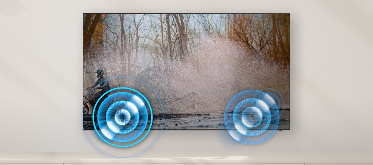 벽에 TV가 설치되어 있으며, 화면에는 산에서 오토바이를 타고 있는 사람의 모습입니다. 왼쪽과 오른쪽 하단에는 동그란 모양의 음향효과가 보입니다.