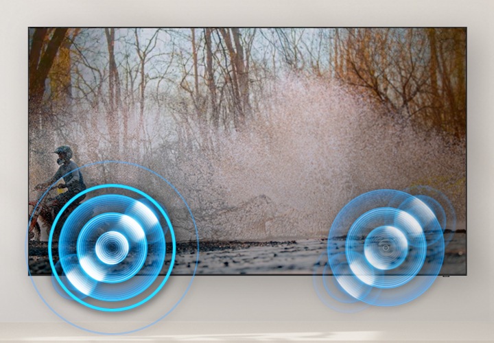 벽에 TV가 설치되어 있으며, 화면에는 산에서 오토바이를 타고 있는 사람의 모습입니다. 왼쪽과 오른쪽 하단에는 동그란 모양의 음향효과가 보입니다.