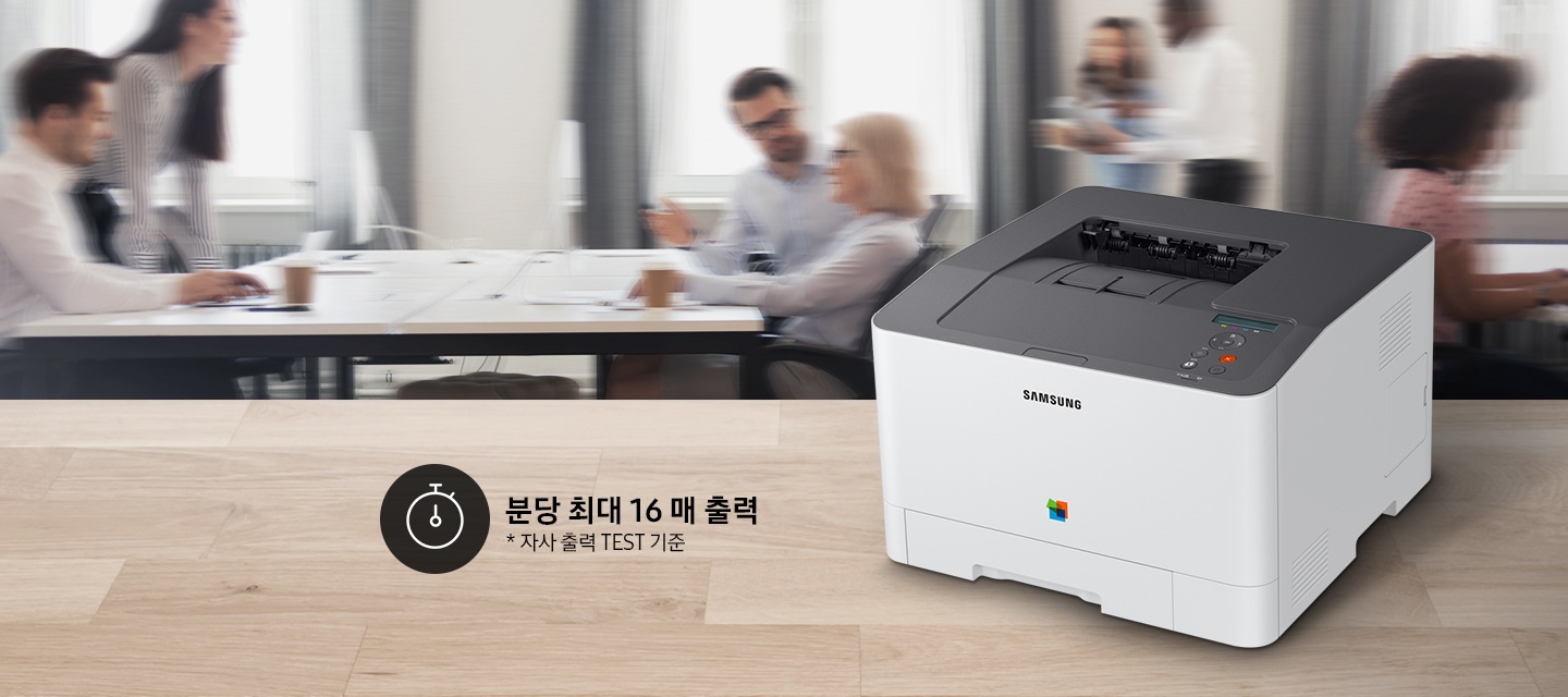 제품이 측면으로 우드 책상 위에 올려져 있고, 그 뒤에는 회의를 하는듯한 배경 이미지가 블러 처리되어 있습니다.