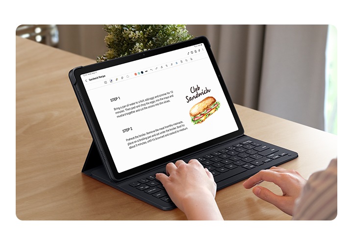 책상 위에 슬림 키보드 북커버를 장착한 갤럭시 탭 A9+로 타이핑하고 있는 모습입니다. 화면에는 클럽 샌드위치 레시피가 표시되고 있습니다.