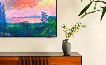 장식장 위에 벽걸이 TV가 설치되어 있고, TV 화면에서는 명화가 보이고 있습니다. 장식장 위에는 화병이 놓여 있습니다.