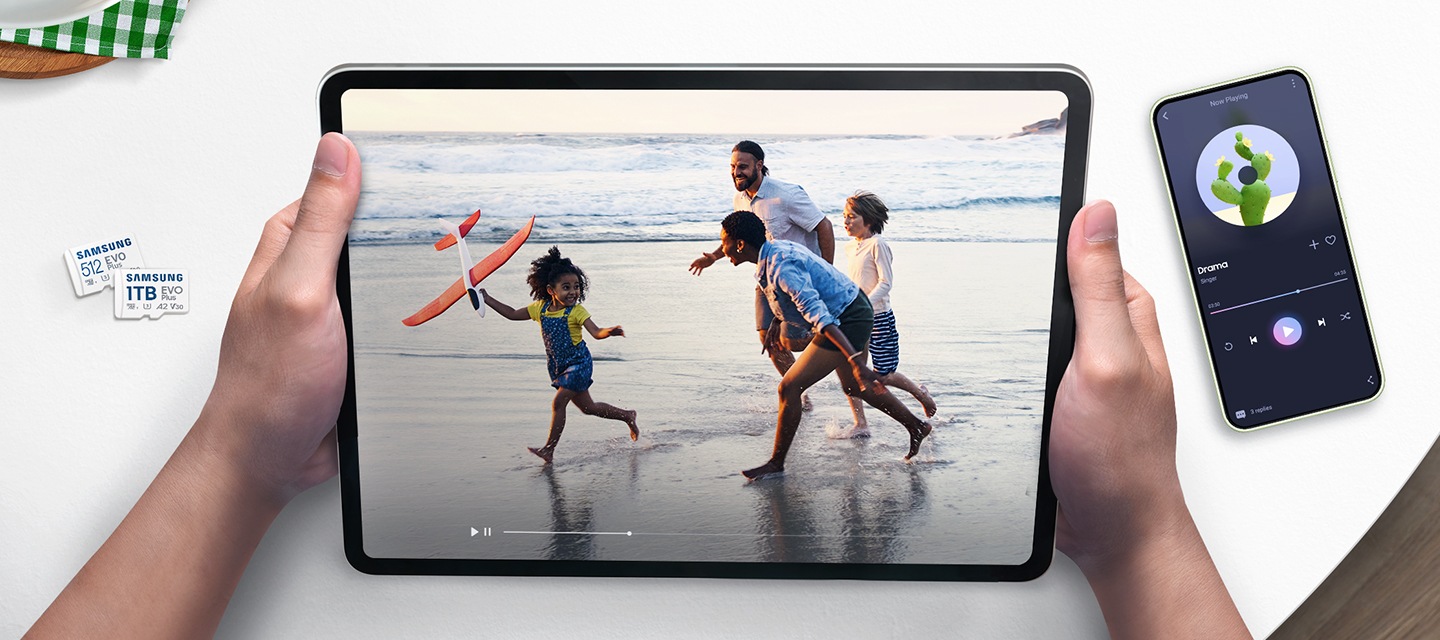 흰색의 책상을 배경으로 이미지 왼쪽 부분에는 메모리카드 정면 모습이 보이고 있고 이미지 중간 부분에는 영상을 재생하고 있는 태블릿을 양손으로 잡고 있는 이미지, 이미지 오른쪽 부분에는 스마트폰에 음악을 재생하고 있는 이미지가 보이고 있습니다.