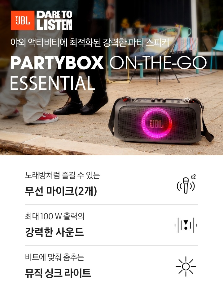 야외에 제품이 놓여 있습니다. 야외 액티비티에 최적화된 강력한 파티 스피커 PARTYBOX ON-THE-GO ESSNTIAL KV입니다. 하단에는 노래방처럼 즐길 수 있는 무선 마이크(2개), 최대 100 W 출력의 강력한 사운드, 비트에 맞춰 춤추는 뮤직 싱크 라이트 문구와 아이콘이 있습니다.