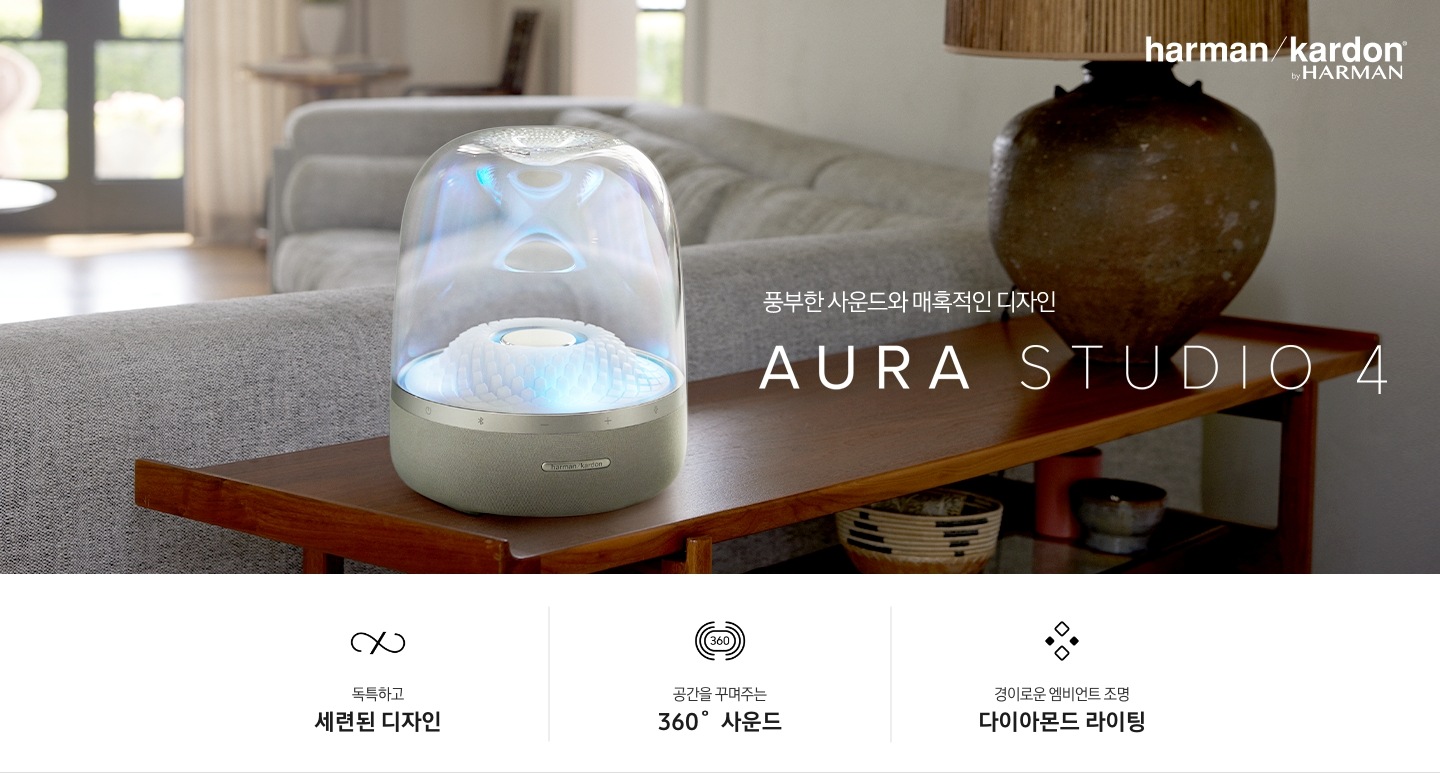 선반 위에 제품이 놓여 있습니다. 제품에는 파란색 불빛이 들어와 있습니다. 제품 오른쪽에는 조명이 있고 뒤에는 소파가 있습니다. 풍부한 사운드와 매혹적인 디자인 AURA STUDIO 4 KV입니다. 하단에는 독특하고 세련된 디자인, 공간을 꾸며주는 360˚ 사운드, 경이로운 엠비언트 조명 다이아몬드 라이팅 문구와 아이콘이 있습니다.