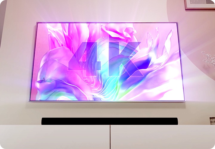 TV 아래 사운드바가 놓여 있습니다. TV 화면에는 분홍색 배경에 4K라고 기재되어 있습니다.