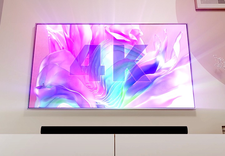 TV 아래 사운드바가 놓여 있습니다. TV 화면에는 분홍색 배경에 4K라고 기재되어 있습니다.