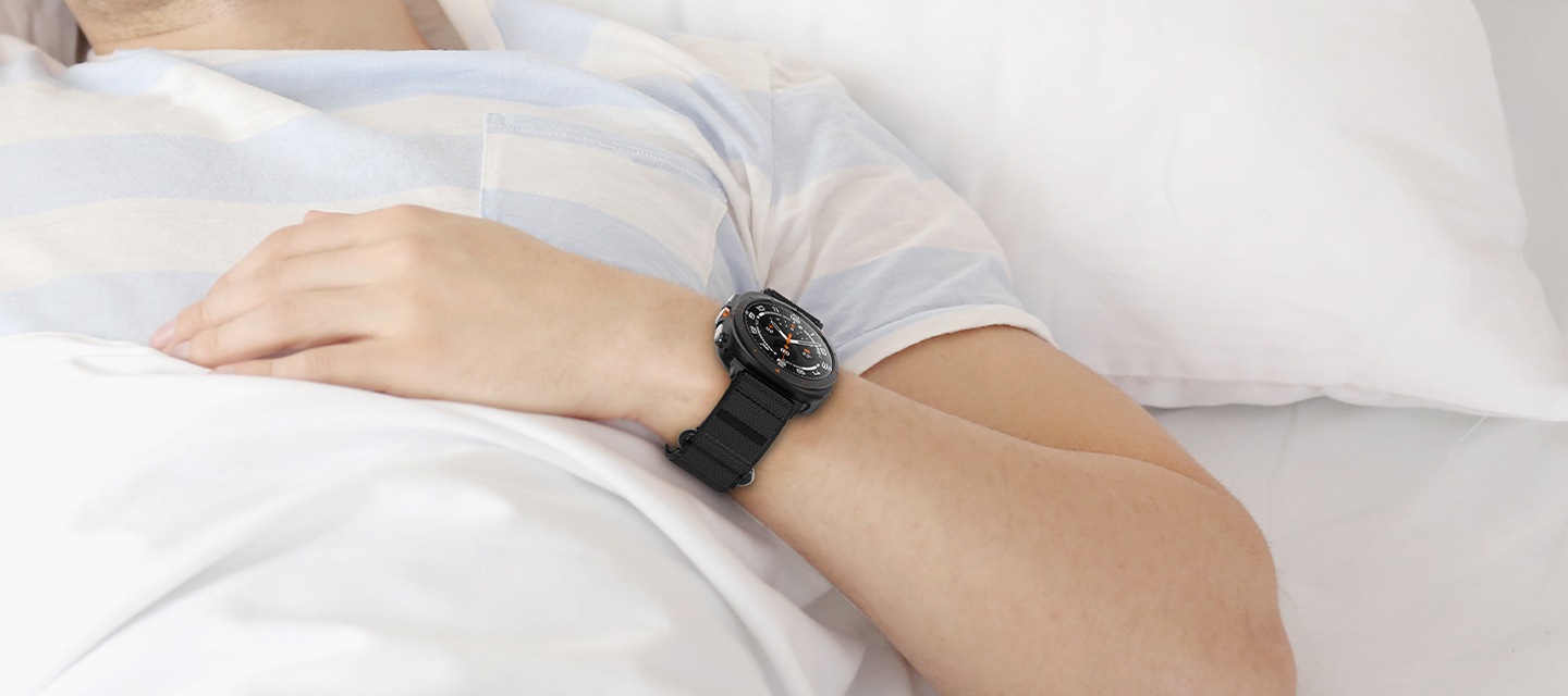 침대에 이불을 덮고 갤럭시 워치 울트라 벨크로 밴드를 착용 후 누워있는 사람의 손목 부분을 확대한 이미지가 보이고 있습니다.