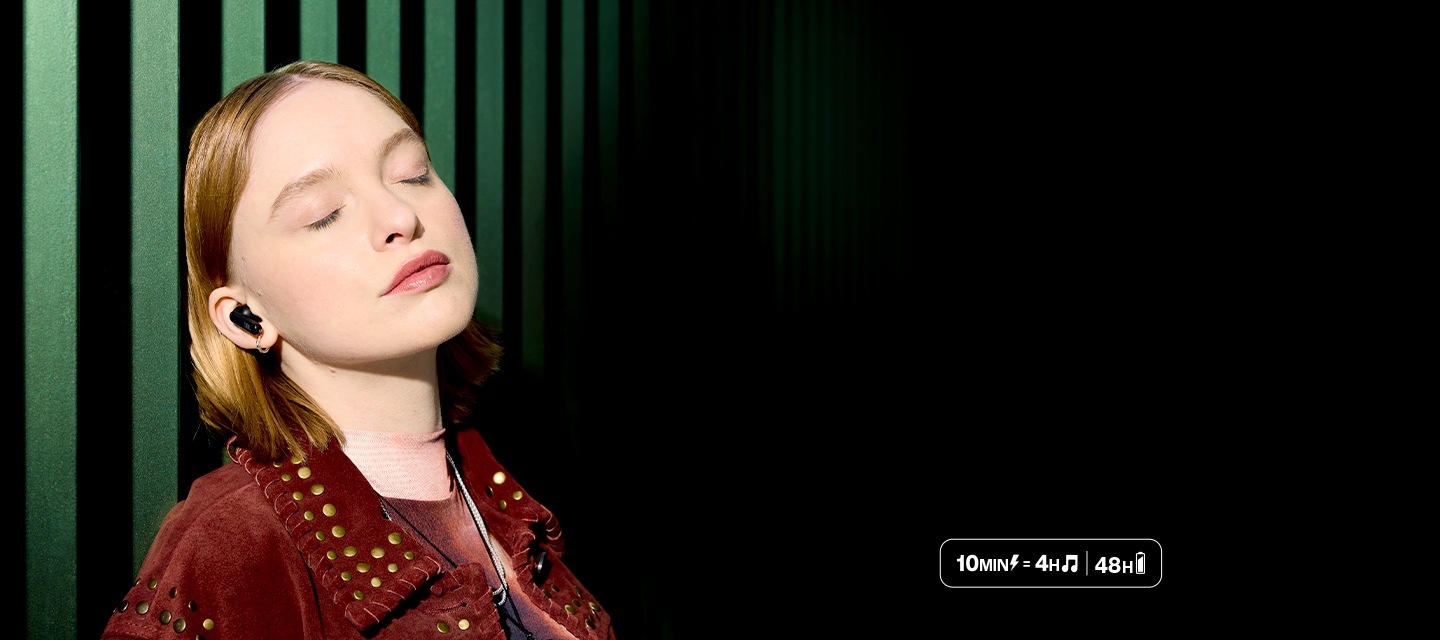 여성이 이어폰을 착용한 상태로 벽에 기대어 있습니다. 