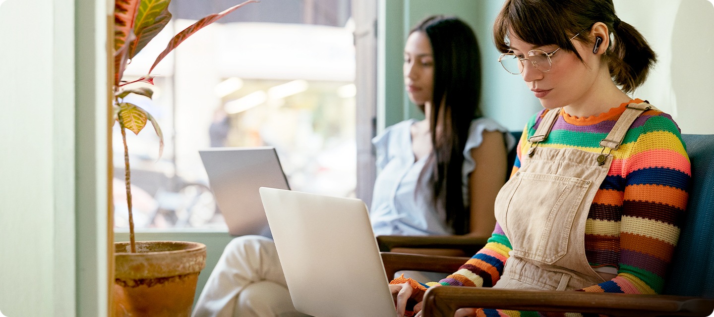 여성이 귀에 이어폰을 착용한 상태로 의자에 앉아서 노트북을 만지고 있습니다.