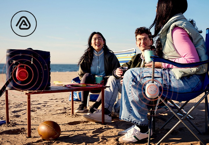 해변에 사람들이 의자를 펴고 앉아 있으며, 청바지를 입은 여성이 앉은 의자 팔걸이에 제품이 걸려 있습니다. 사람들 앞에는 테이블이 있습니다. 테이블 위에는 가방이 올려져 있으며, 가방 끈에는 제품이 걸려 있습니다. 