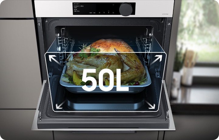 그레이 계열의 장과 우측엔 창밖 나무가 보이는 주방 환경 인테리어 가운데에 글램 화이트 색상의 오븐이 배치되어 있습니다. 오븐은 정면으로 오픈되어 있으며, 50L 용량으로 대용량 음식을 조리할 수 있는 문구 및 구조를 표현하고 있습니다. 열려있는 오븐 내에는 익혀진 통닭이 플레이팅 되어 있습니다.