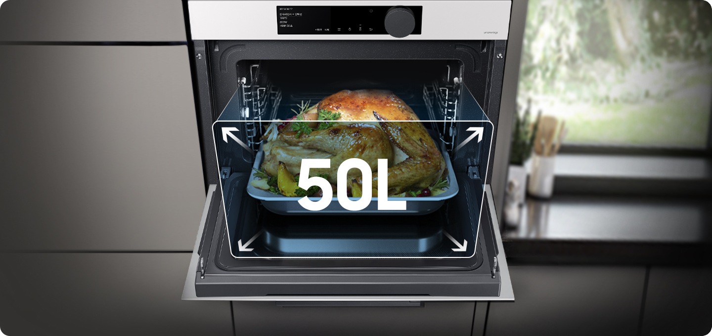 그레이 계열의 장과 우측엔 창밖 나무가 보이는 주방 환경 인테리어 가운데에 글램 화이트 색상의 오븐이 배치되어 있습니다. 오븐은 정면으로 오픈되어 있으며, 50L 용량으로 대용량 음식을 조리할 수 있는 문구 및 구조를 표현하고 있습니다. 열려있는 오븐 내에는 익혀진 통닭이 플레이팅 되어 있습니다.