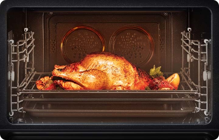 요리 및 작동이 되고 있는 오븐의 오픈된 상태가 보여집니다. 오븐 내에는  통닭과 마늘, 레몬 등 각종 야채가 거의 다  익혀진 이미지 입니다.