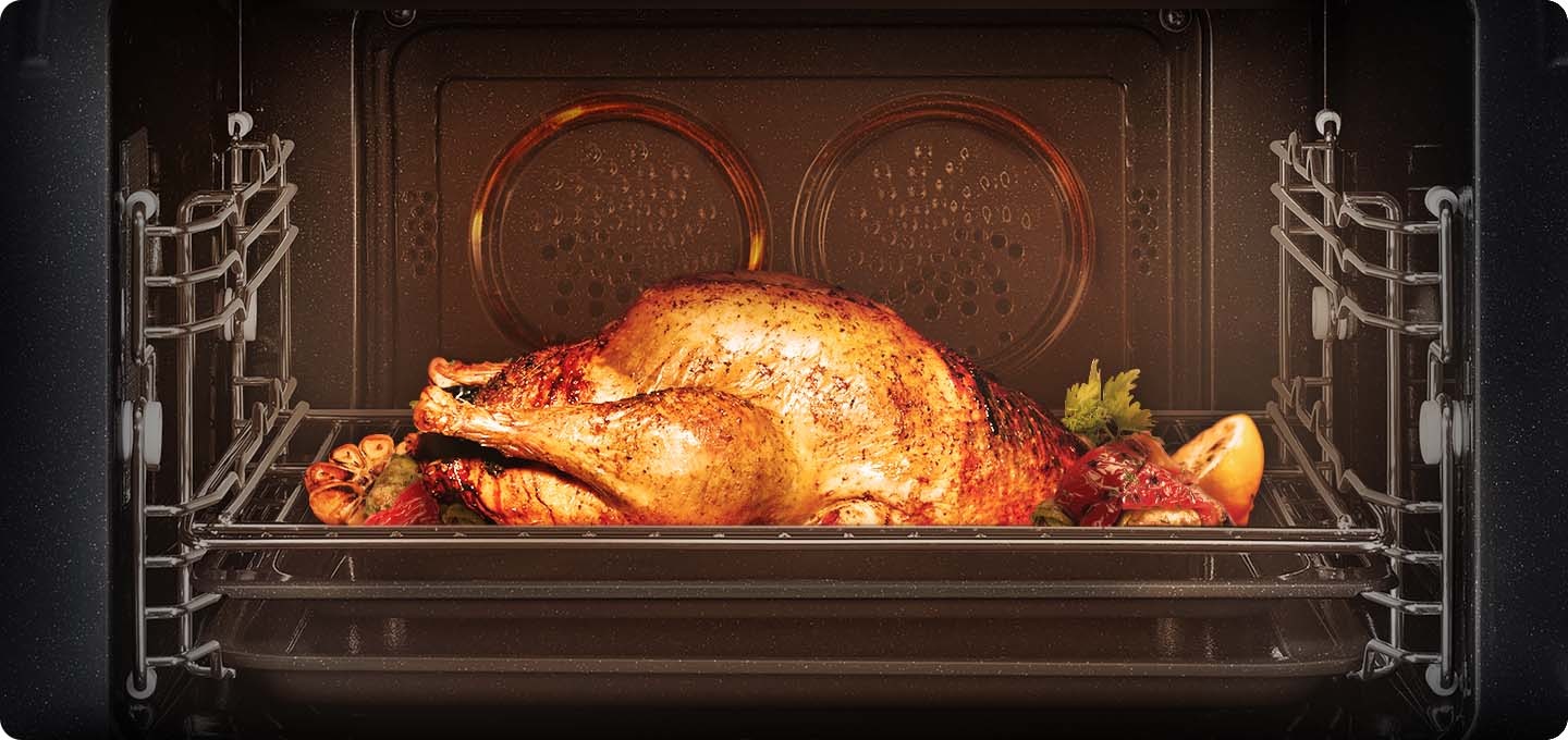 요리 및 작동이 되고 있는 오븐의 오픈된 상태가 보여집니다. 오븐 내에는  통닭과 마늘, 레몬 등 각종 야채가 거의 다  익혀진 이미지 입니다.