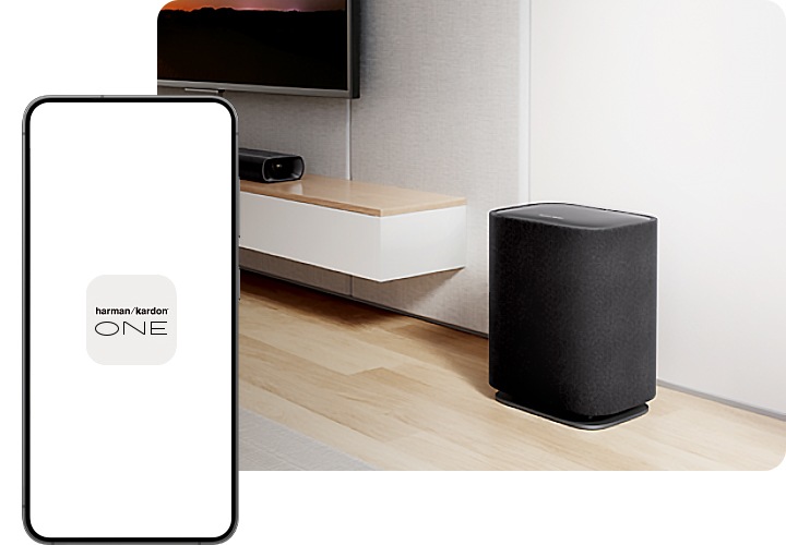 거실에 제품이 설치되어 있습니다. 그 앞에는 화면에 Harman Kardon One 앱 아이콘이 노출된 스마트폰이 있습니다.