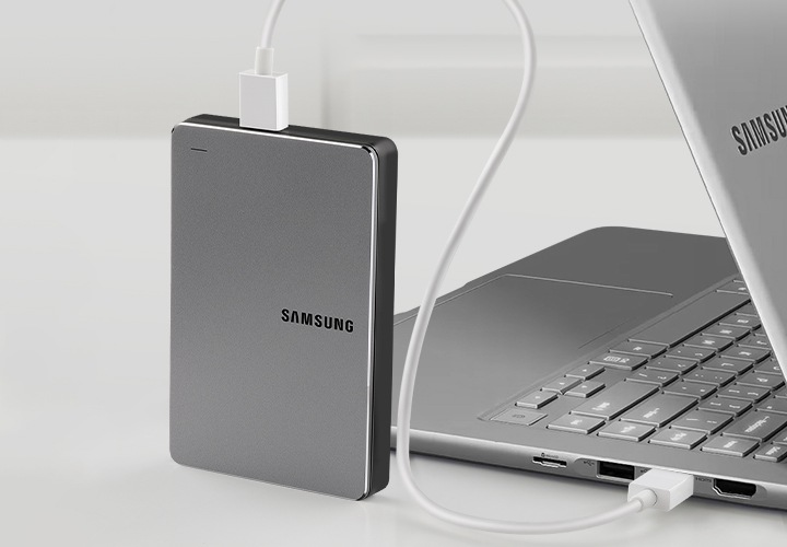 하얀색 배경에 이미지 오른쪽 부분에는 노트북이 70도만 열린 제품 옆면 이미지가 보이고 있고 이미지 왼쪽에 노트북과 케이블로 연결된 외장 HHD 4TB 제품이 세로로 세워져 있습니다.