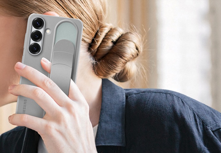 한 여성이 그레이 색상의 스탠딩 그립 케이스가 장착된 갤럭시 S25를 들고 있습니다. 한 손가락이 그립 아래에 끼워져 있습니다.