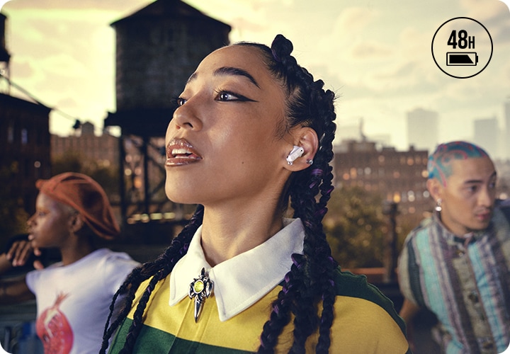 화이트 색상의 이어버드를 착용한 여성이 보입니다. 뒤에는 춤을 추고 있는 사람이 보입니다.