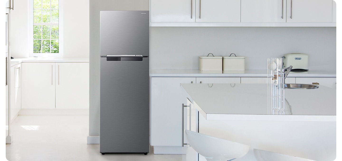 화이트톤의 주방 인테리어컷 입니다. 냉장고 좌측에 창문이 있고 밖으로는 초록색 나뭇잎이 보이며, 아래에 흰색 하부장이 있습니다. 중앙에 냉장고가 놓여있고 우측으로는 화이트톤의 상하부장이 있고 다양한 오브제가 놓여있습니다.