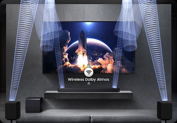 벽에 TV가 설치되어 있으며, 하단 장식장에는 사운드바가 설치되어 있습니다. 장식장 왼쪽 아래에는 서브 우퍼가 놓여 있고, 소파 양 옆에는 무선 리어 스피커가 설치되어 있습니다. 사운드바와 무선 리어 스피커에서 음향효과가 나오고 있습니다.