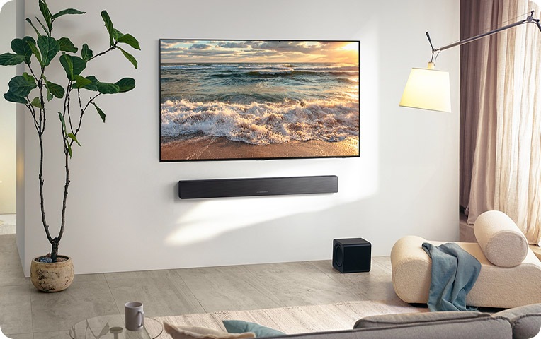 거실 벽에 TV와 사운드바가 설치되어 있으며, 바닥에는 서브 우퍼가 놓여 있습니다.