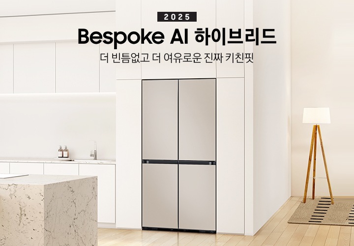 2025 Bespoke AI 하이브리드. 더 빈틈없고 더 여유로운 진짜 키친핏. 화이트톤의 주방 인테리어컷으로 냉장고장에 4도어 냉장고가 설치되어 있습니다. 냉장고 좌측으로는 동일한 화이트톤 상하부장과 수전, 오브제가 나와있으며 우측으로는 스탠드 조명이 나와있고 앞쪽에는 대리석 아일랜드 식탁이 나와있는 이미지 입니다.