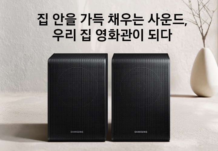 무선 리어스피커가 놓여 있습니다. 스피커 뒤로는 화병이 보입니다. 집 안을 가득 채우는 사운드, 우리 집 영화관이 되다. 무선 리어스피커 KV입니다.