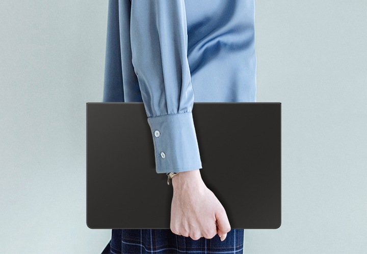파란색 셔츠를 입은 사람이 슬림 키보드 북커버를 장착한 갤럭시 탭 S10 FE+를 들고 걸어가고 있습니다.
