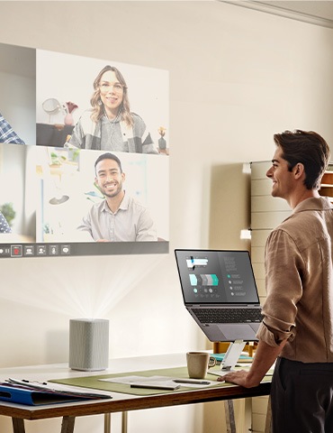 남성이 책상 위에 설치된 프로젝터로 화상회의를 하고 있습니다.