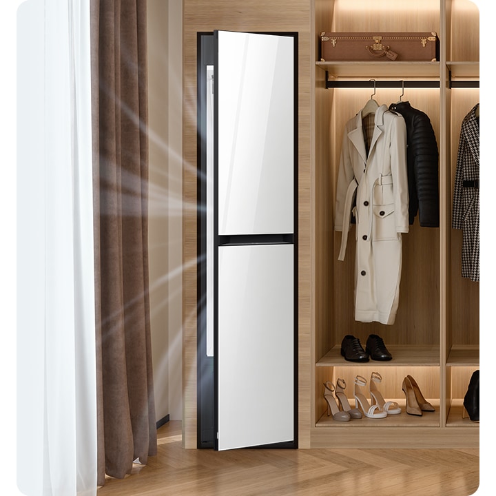 따뜻한 톤의 행거옷장이 좌측에 있고 옷걸이에는 옷이 두벌 걸려있습니다, 옷 위로는 캐리어 가방 있고, 아래에는 여러 개의 구두있습니다. 바로 옆 우측에는 에어드레서 드레스룸을 제습하고 있는 모습입니다.