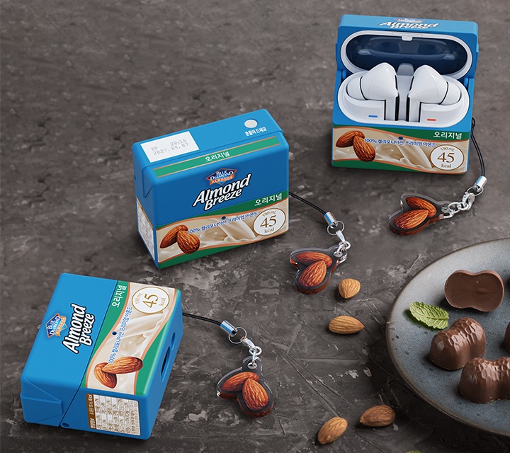 가장 우측에 버즈에 장착된 아몬드 브리즈 오리지널 케이스가 뚜껑이 열린 채 세워져 있고, 그 좌측는 뚜껑이 닫힌 케이스가 세워져 있으며, 가장 좌측에 뚜겅이 닫힌 케이스가 눕혀져 있습니다.