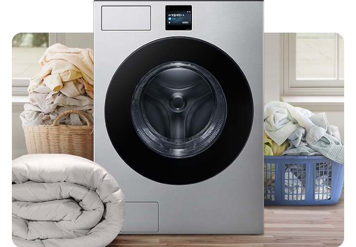 Bespoke AI 세탁기가 중앙에 나와있고 좌측 뒷편 라탄 바구니에 의류가 가득 쌓여있고 앞쪽에 이불이 나와있습니다. 우측 파란색 플라스틱 바구니에도 수건 등 각종 옷감이 가득 쌓여있는 연출된 이미지입니다.