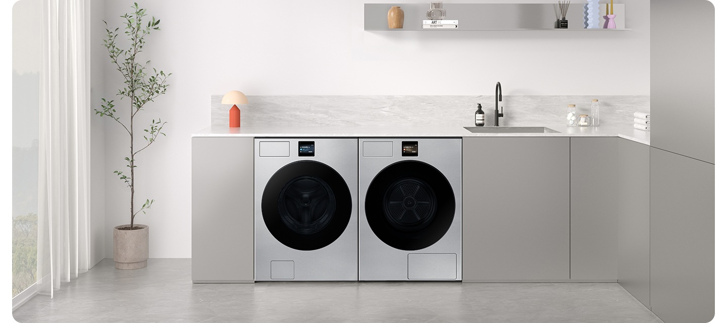 그레이톤 하부장에 세탁기와 건조기가 병렬로 설치되어 있습니다. 하부장 위에는 각종 오브제가 작은 싱크대가 설치되어 있는 연출된 이미지입니다.