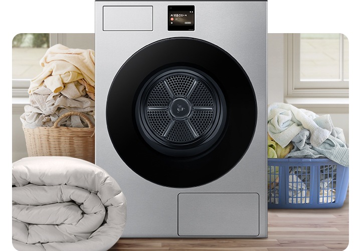 Bespoke AI 건조기가 중앙에 나와있고 좌측 뒷편 라탄 바구니에 의류가 가득 쌓여있고 앞쪽에 이불이 나와있습니다. 우측 파란색 플라스틱 바구니에도 수건 등 각종 옷감이 가득 쌓여있는 연출된 이미지입니다.