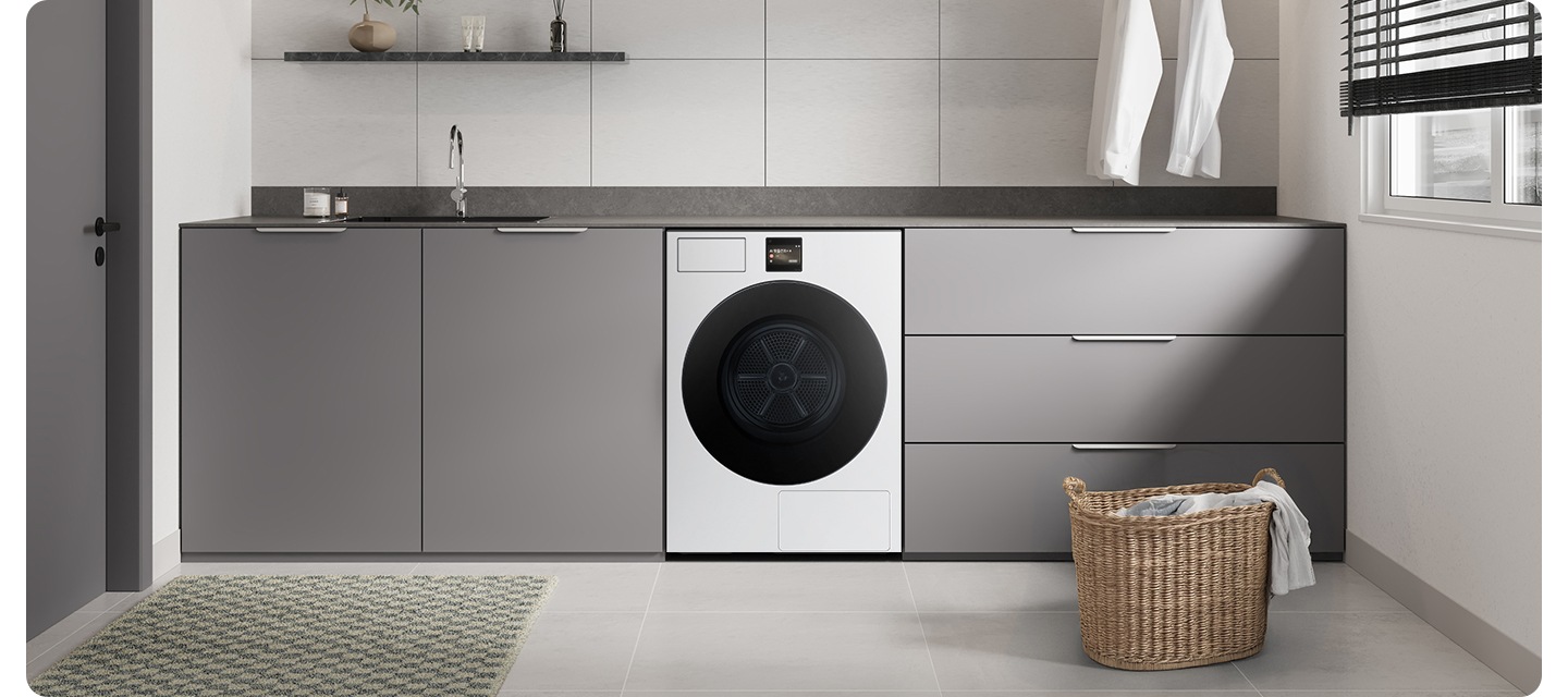 화이트&그레이톤 인테리어컷으로 그레이톤 하부장 중앙에 Bespoke AI 건조기가 설치되어 있습니다. 상부장 부분에는 싱크대와 수전이 있고 앞쪽에는 라탄 바구니에 옷감이 들어있는 연출된 이미지입니다.