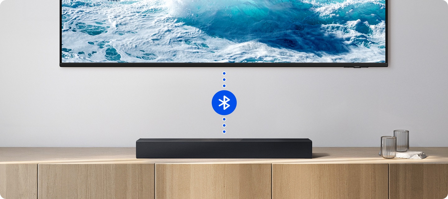 거실 벽에 TV가 설치되어 있습니다. TV와 사운드바가 연결되어 있고 블루투스 아이콘이 보입니다.