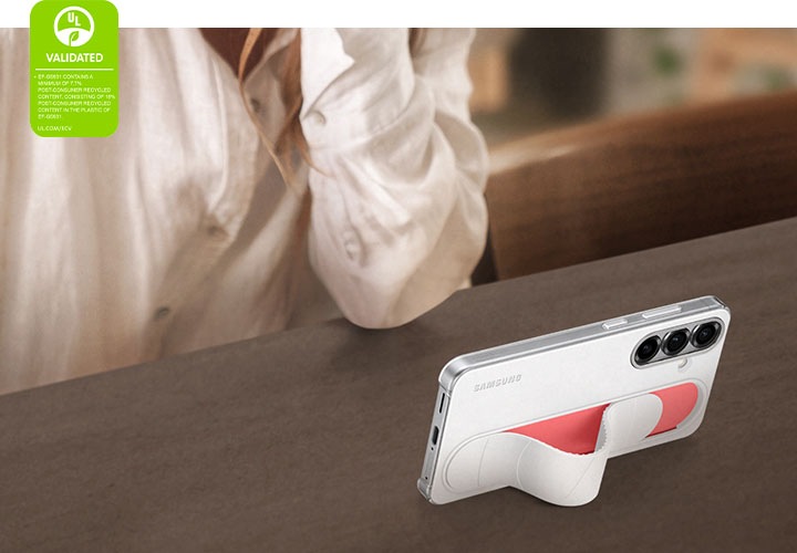 흰색 스탠딩 그립 케이스를 장착한 갤럭시 S25가 기울어진 채 서있습니다. 가로모드로 영상이 재생됩니다. 왼쪽 모서리에는 '스탠딩 그립 케이스는 최소 7.7%의 소비자 재활용 콘텐츠를 포함하고, 케이스에 사용된 플라스틱에는 18% 소비자 재활용 콘텐츠를 포함합니다. UL.COM/ECV' 라고 적힌 UL 환경 클레임 검증 마크가 표시되어 있습니다.