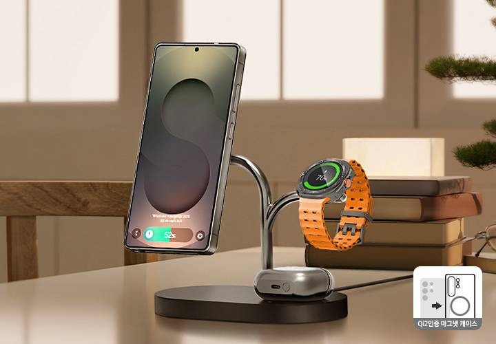 [책상 위에 뒷쪽 부분에는 책 더미와 안경, 연필, 조경 식물이 놓여 있고, 그 앞에 갤럭시 스마트폰, 갤럭시 워치, 갤럭시 버즈를 동시에 충전하고 있는 제품이 보이고 있습니다.]