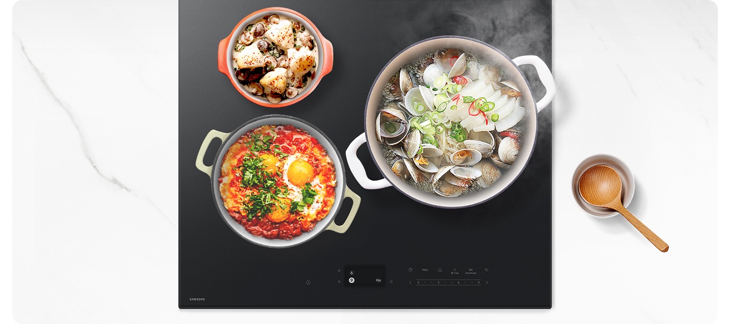 [흰색대리석 상판 위 Íñfí~ñíté~ Líñé~ 전기 레인지가 정면으로 보입니다. 화구에는 크기가 다른 3개의 냄비에 음식물이 가득 들어있는 상태로 올려져 있습니다. 우측 대화구에는 가장 큰 흰색 냄비와 조개와 무가 가득 들은 조개탕이 펄펄 끓고 있는 모습입니다. 플렉스 존 상단에는 가장 작은 사이즈의 오렌지색 냄비와 크림수프가 완성되어 있습니다. 플렉스 존 하단에는 중간 사이즈의 연두색 냄비에 에그인 헬이 완성되어 있습니다. 전기레인지 오른쪽에는 흰색 도자기 그른 안에 나무 주걱이 들어 있습니다.]