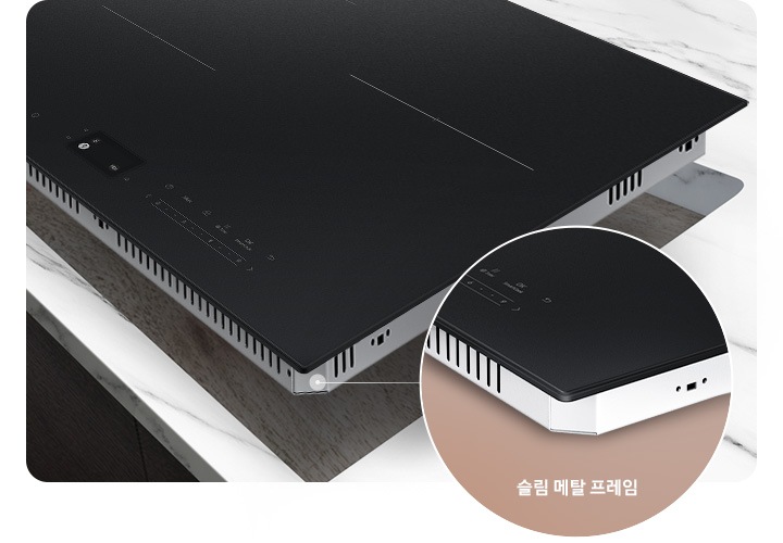 [진한 갈색의 마루가 깔린 바닥이 보이고 어두운 갈색 패널의 주방 위 흰색대리석 상판이 깔린 주방 테이블이 보입니다. 그 위에 전기레인지 부위가 타공되어 있고, 타공 된 위치 조금 위로 전기 레인지가 보입니다. 전기레인지 오른쪽 하단에는 닷 모양의 표시와 함께 원형으로 프레임 부분이 확대되어 보입니다. 확대된 프레임 하단에는 슬림 메탈 프레임이라는 문구가 적혀 있습니다.]