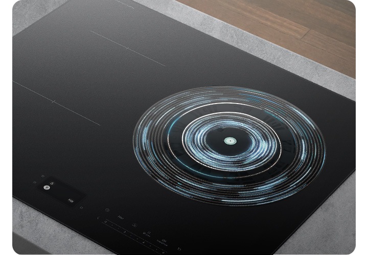 [오른쪽 상단에는 진한 갈색의 마룻 바닥이 보입니다. 그 아래 회색 상판이 깔린 주방 테이블 위로 전기 레인지가 설치되어 있는 모습이 보입니다. 전기 레인지의 오른쪽 화구의 가열 영역이 파란색 선들로 원형으로 표현되어 있습니다.]